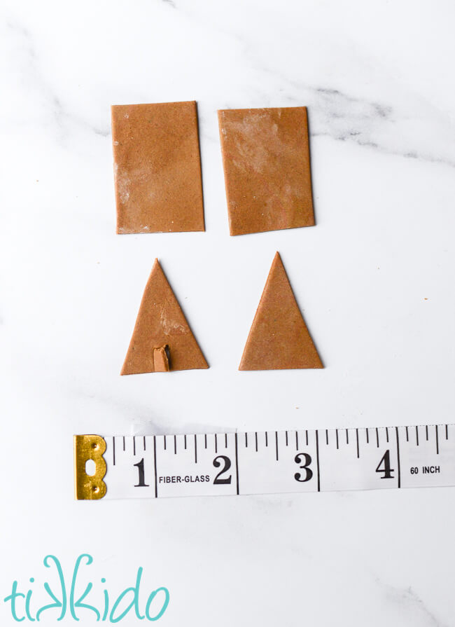Miniature A-frame gingerbread house pieces next to a ruler for scale.