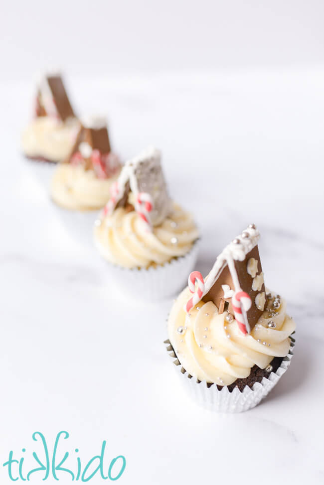 Line of Christmas cupcakes with miniature gingerbread house cupcake toppers.