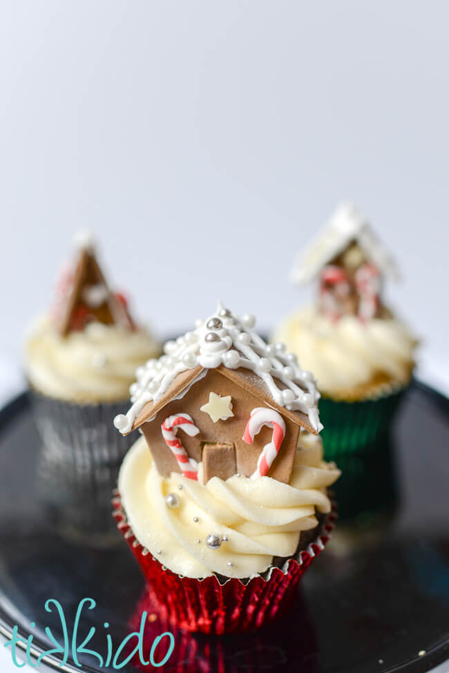 Three Christmas cupcakes topped with miniature gingerbread house cupcake toppers.