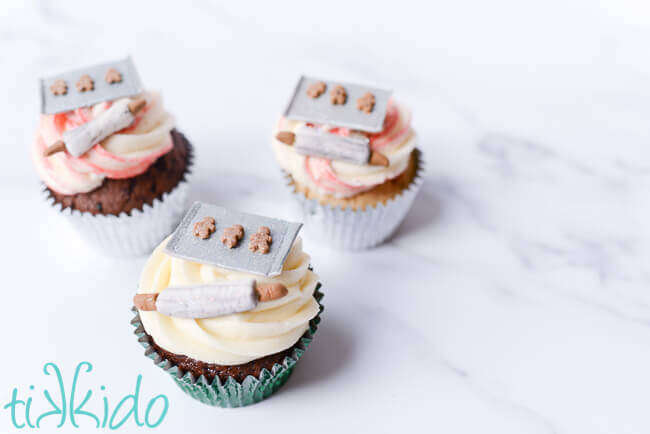 Three Christmas baking scene cupcakes topped with miniature rolling pins and cookie sheets made out of gum paste.