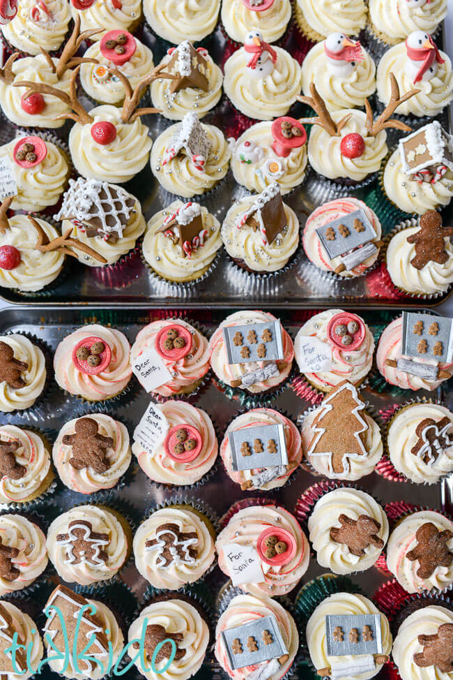 Large collection of Christmas cupcakes on silver baking trays.