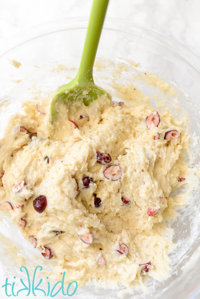 Cranberry muffins batter in a clear bowl with a green spatula.