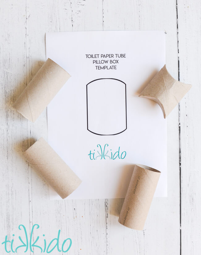 Printable toilet paper roll pillow box template surrounded by toilet paper tubes, one of which has been shaped into a pillow box.