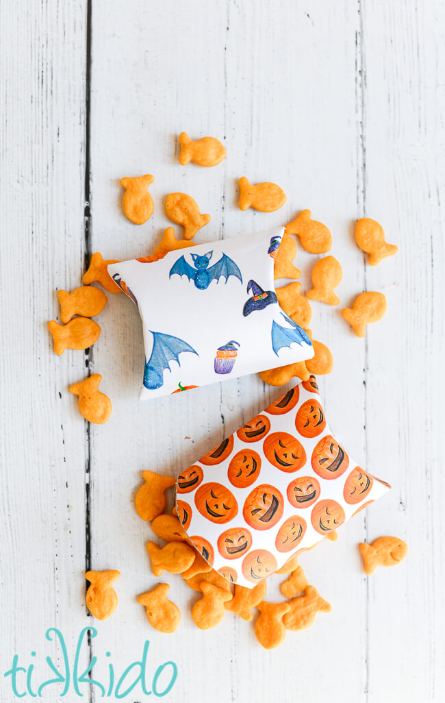 DIY Pillow Boxes covered in printable Halloween papers, surrounded by goldfish crackers on a white wooden background.