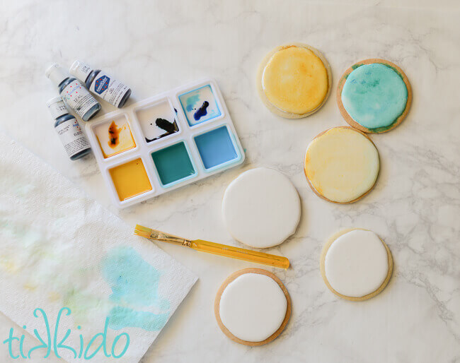 Sugar cookies iced with white icing, and being painted with food coloring using watercoloring techniques.