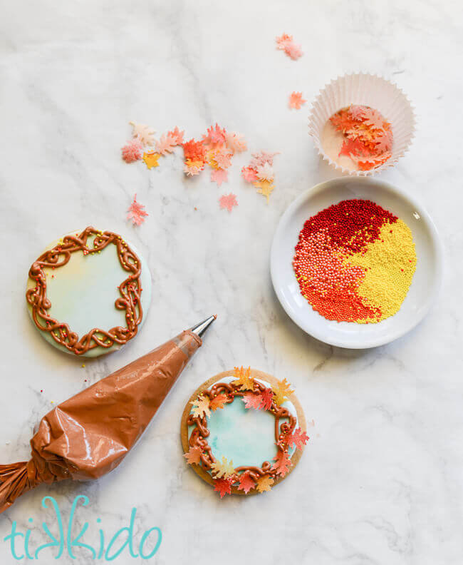 Sugar cookies being decorated to look like fall wreaths, complete with edible wafer paper fall leaves.