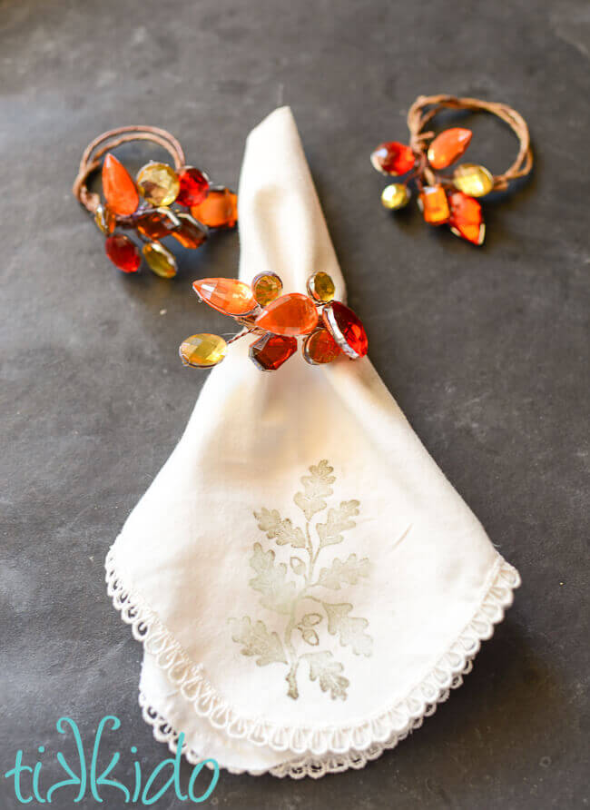 Jeweled napkin rings in fall colors on a fabric napkin on a black chalkboard background.