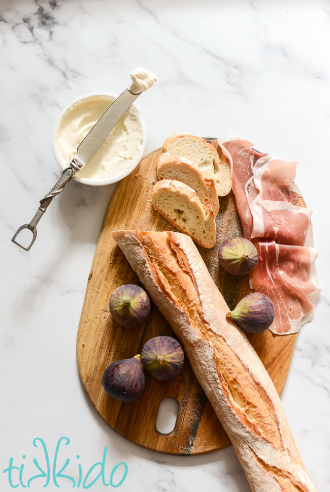 Ingredients for Fig, Prosciutto, and Mascarpone Crostini on a wooden cutting board.