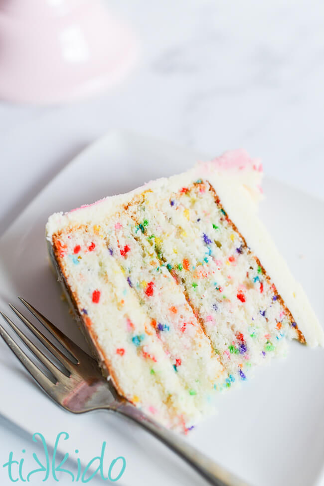 Slice of the best funfetti cake recipe on a white plate next to a fork.