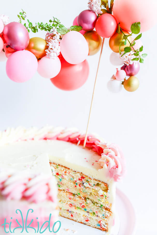 Funfetti cake with a slice cut out of it so you can see the colors of the sprinkles baked into the cake.