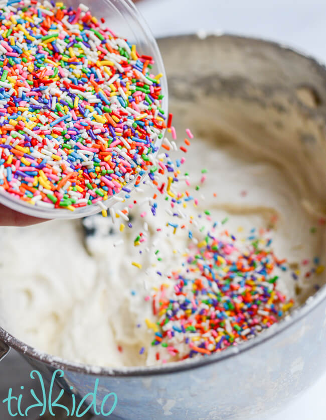 Rainbow sprinkles being poured into white cake batter to make funfetti cake.