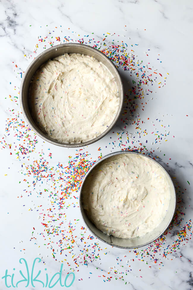 Funfetti cake batter in two 8" round cake pans, with rainbow sprinkles surrounding the pans.