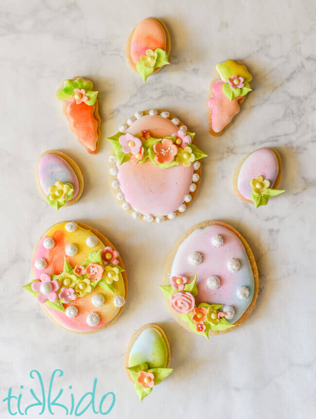 Easter egg and carrot watercolor sugar cookies with royal icing flowers on a white marble background.