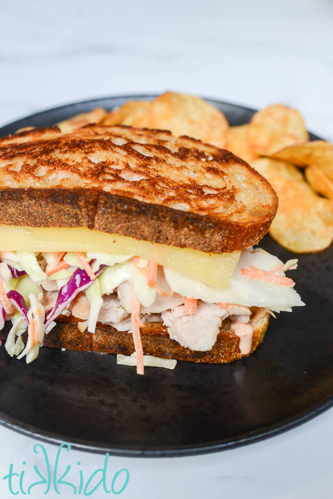 Closeup of a Georgia Reuben sandwich, made with turkey and coleslaw, on a black plate with chips.