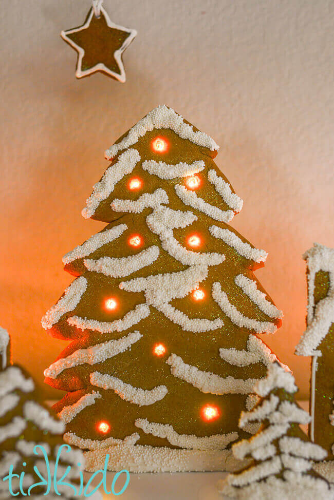 Standing gingerbread Christmas tree decorated with white royal icing and white sprinkles and lit up with LED battery operated lights.