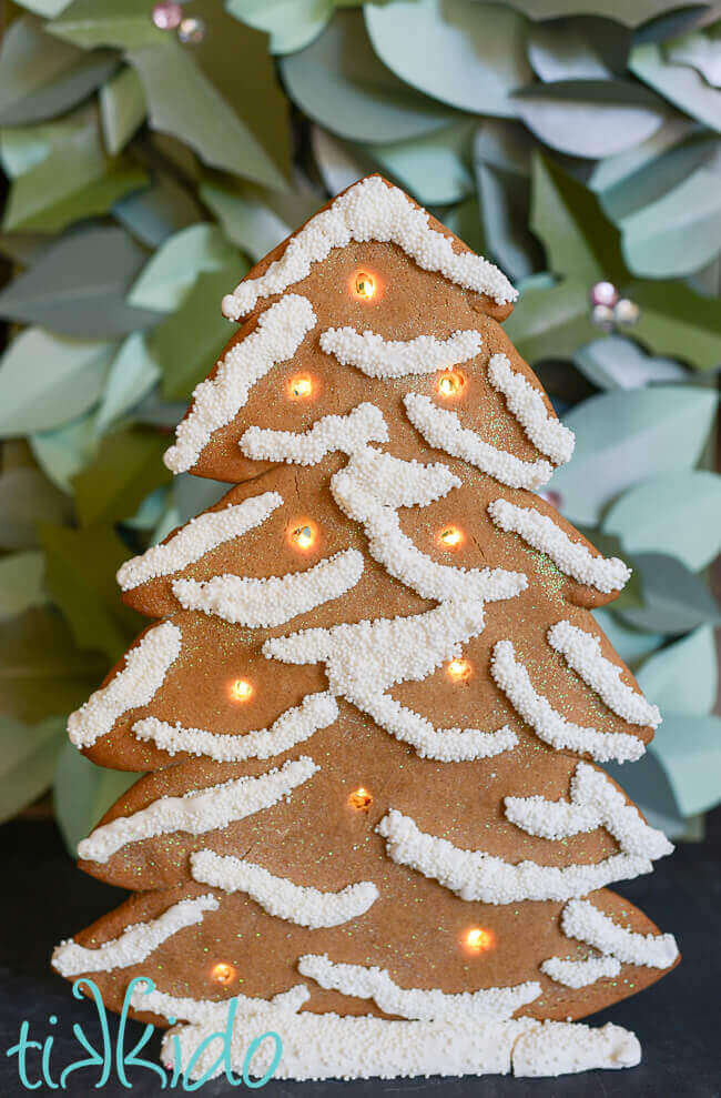 Standing gingerbread Christmas tree decorated with white royal icing and white sprinkles and lit up with LED battery operated lights.