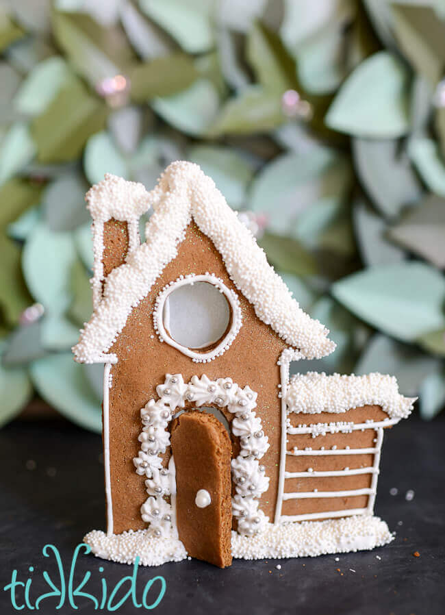 Gingerbread house candle holder decorated with white royal icing and sprinkles.