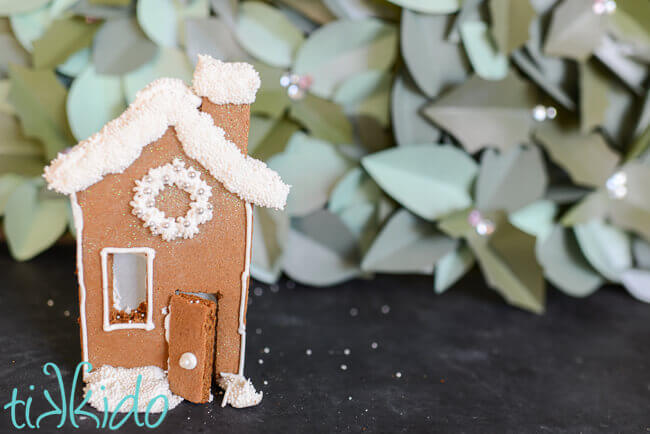 Small gingerbread house candle holder in front of a green paper background.