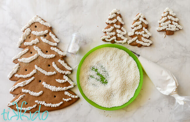 Gingerbread trees being decorated with royal icing and white sprinkles.