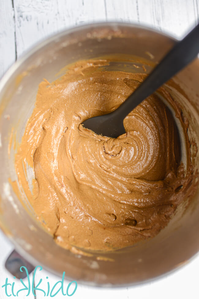 Batter for gingerbread quick bread and a black spatula in a Kitchenaid mixing bowl on a white wooden surface.