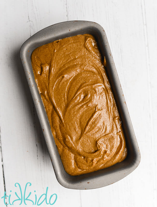 Gingerbread loaf batter in a bread pan on a white wooden surface.