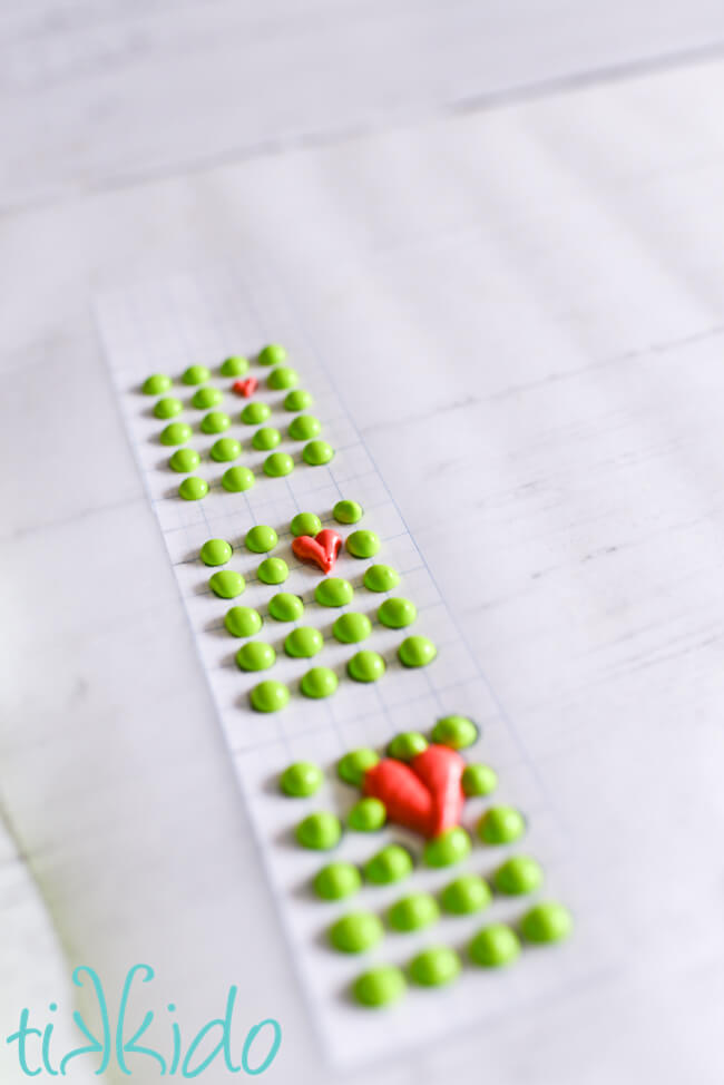 Grinch Candy Buttons piped on wax paper over a template drawn on graph paper.