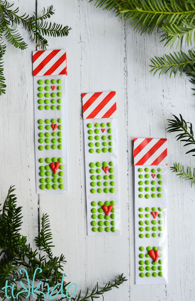 Three packages of Grinch themed homemade candy buttons on a white wooden background.