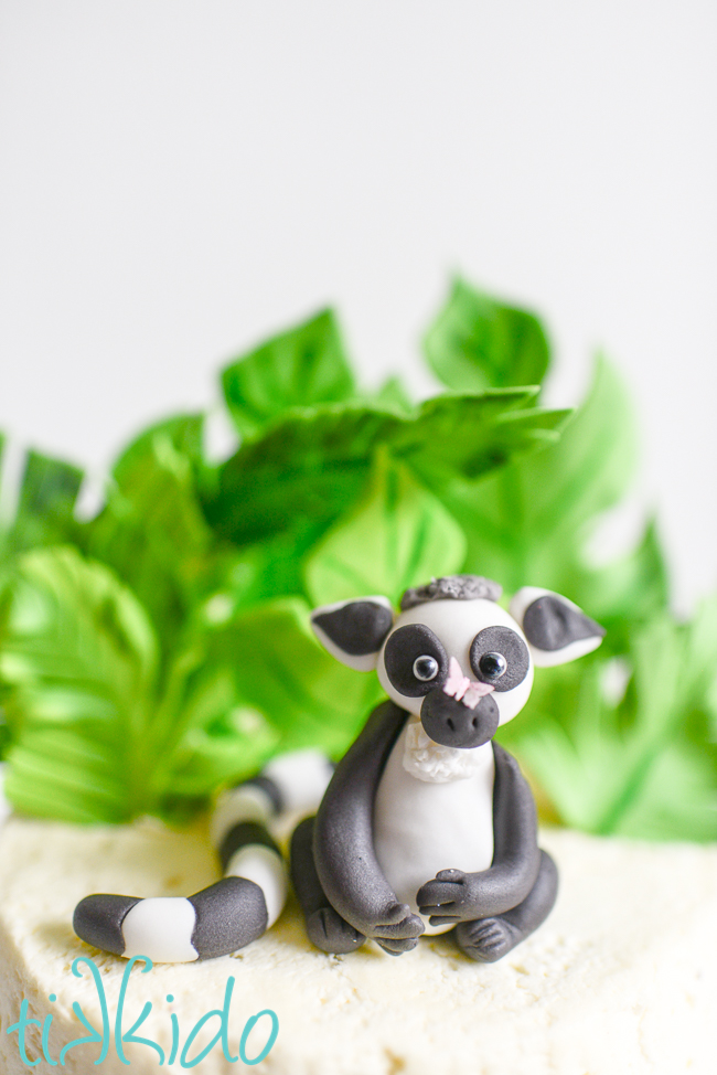 Gum paste lemur with a tiny butterfly sitting on his nose, sitting on top of a birthday cake.