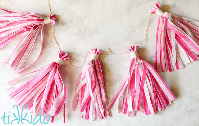 Pink striped tissue paper tassel garland made from napkins on a white marble surface.