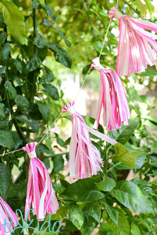 DIY tissue paper tassel garland made from pink napkins hanging in a tree.