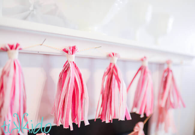 Pink DIY tassel garland made from napkins on a white fireplace mantle.