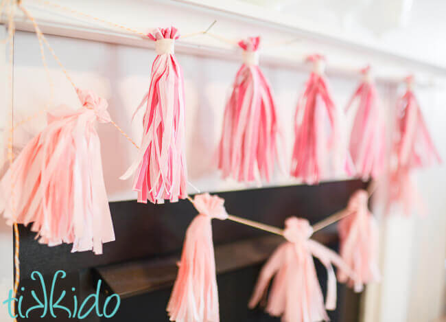 Pink tissue paper tassel garland made from napkins on a white fireplace mantle.