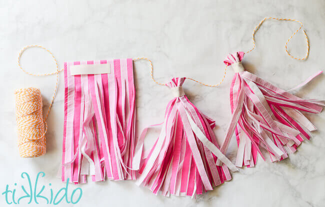 Striped pink paper napkins being turned into tissue paper tassels on a garland.