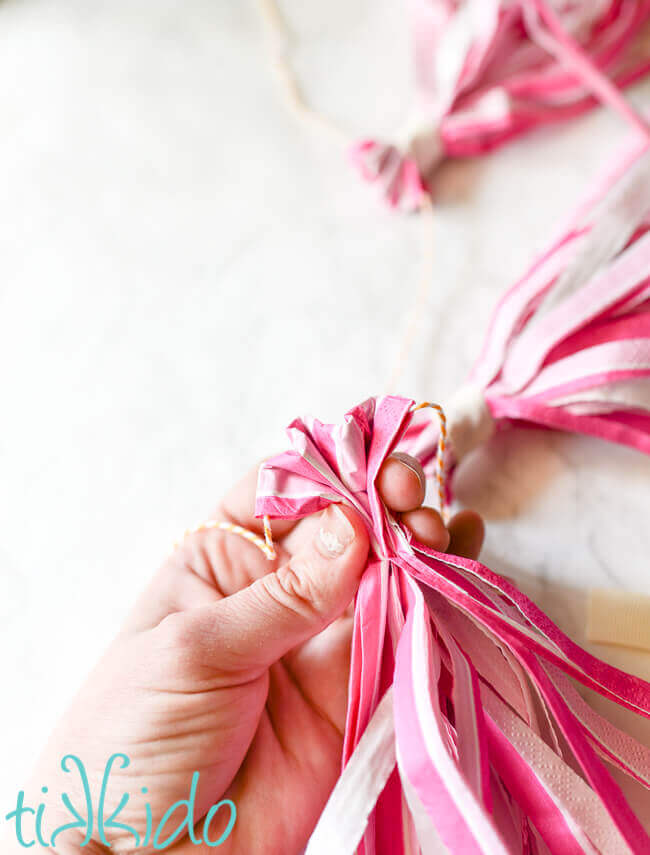 Pink striped napkin cut into fringe and being gathered into a tassel shape.