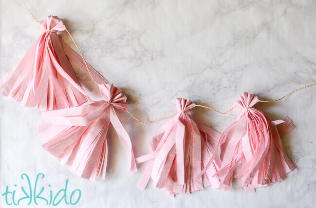 Light pink tissue paper tassel garland made from napkins on a white marble surface.