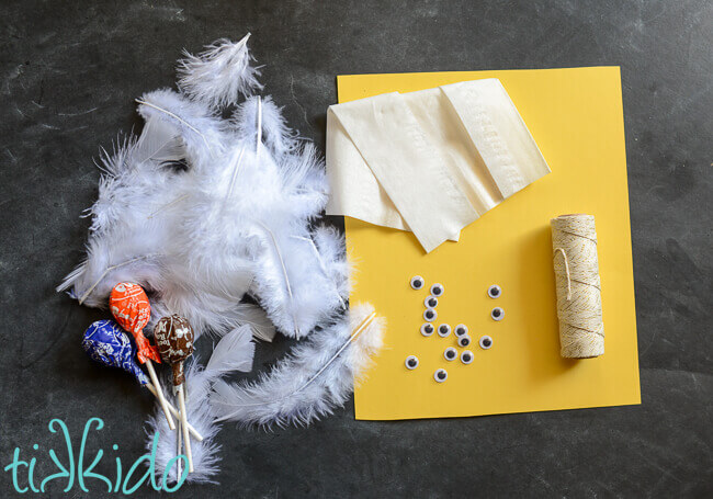 lollipops, feathers, tissue paper, string, yellow paper, and googly eyes on a black background.