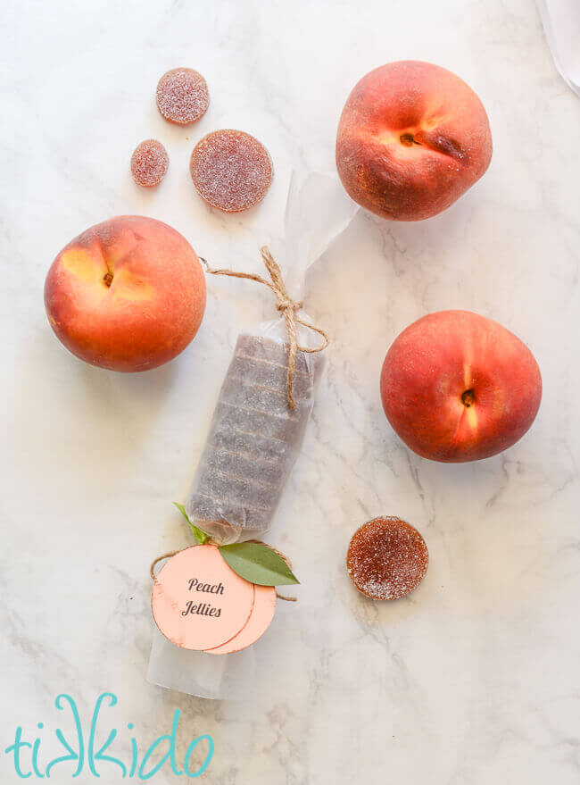 Peach pate de fruits candies and fresh peaches on a white marble surface.