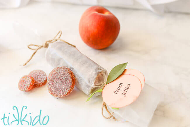 Peach jellies candies (Pate de fruit) next to a fresh peach on a white marble surface.