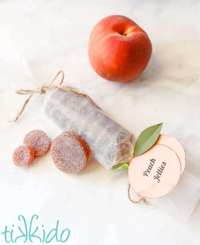 Peach jellies candies (Pate de fruit) next to a fresh peach on a white marble surface.
