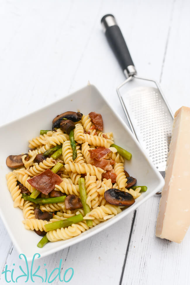 Bowl of Prosciutto, Asparagus, Mushroom pasta next to a block of parmesan cheese and cheese grater.