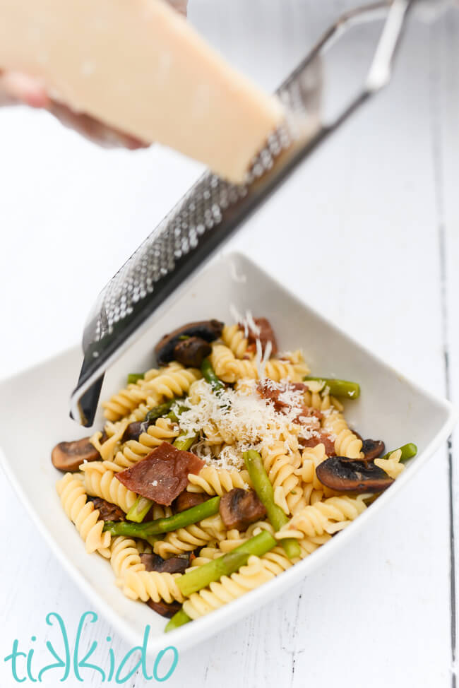 Prosciutto, asparagus, mushroom pasta being topped with freshly grated parmesan cheese.