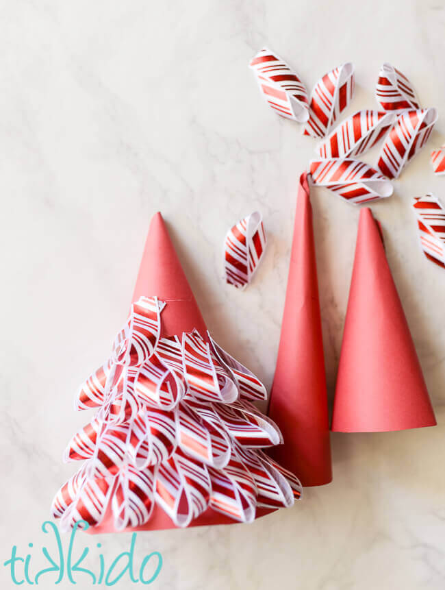 Ribbon being glued to a red paper cone to create peppermint striped ribbon Christmas tree decorations.
