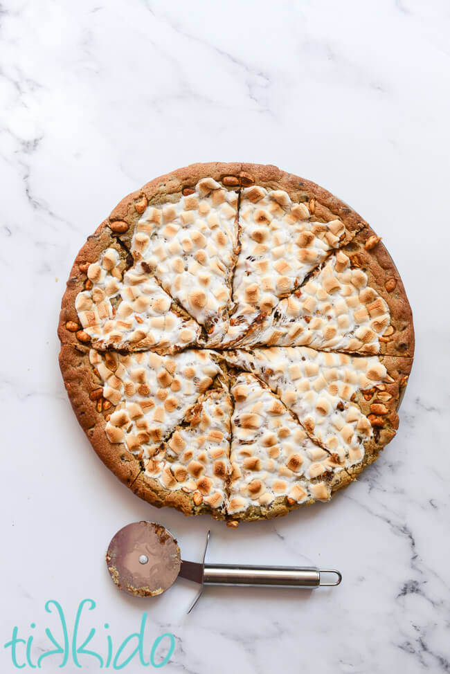 Pizza Cookie (pizookie) cut into slices with a pizza cutter, on a white marble surface.
