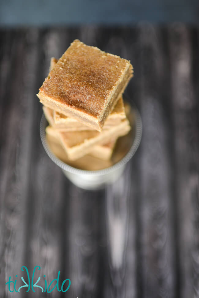 Top down view of four stacked squares of cut snickerdoodle bar cookies sitting on a small silver tray, on a dark wooden surface.