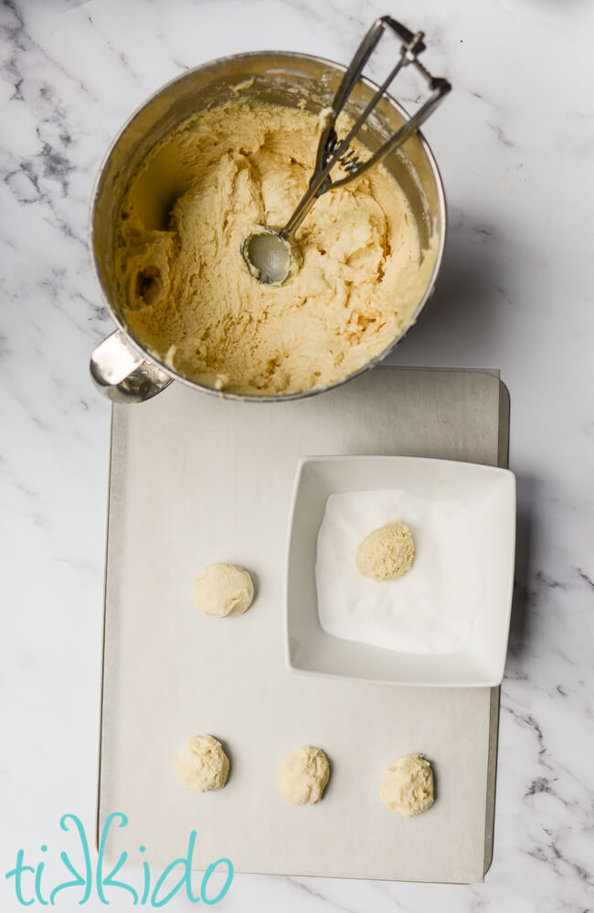 Soft sugar cookies being scooped out and rolled in sugar before baking.