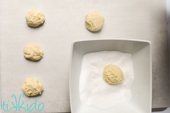 Soft sugar cookies being scooped out and rolled in sugar before baking.