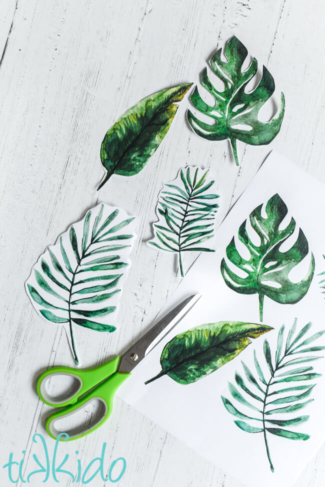 Printable tropical leaves cut out on a white wooden background.