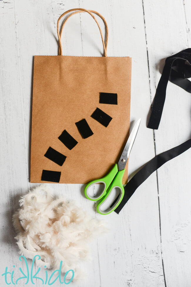 Black velvet ribbon cut into pieces and arranged into a curving lemur tail shape on a plain brown kraft gift bag.