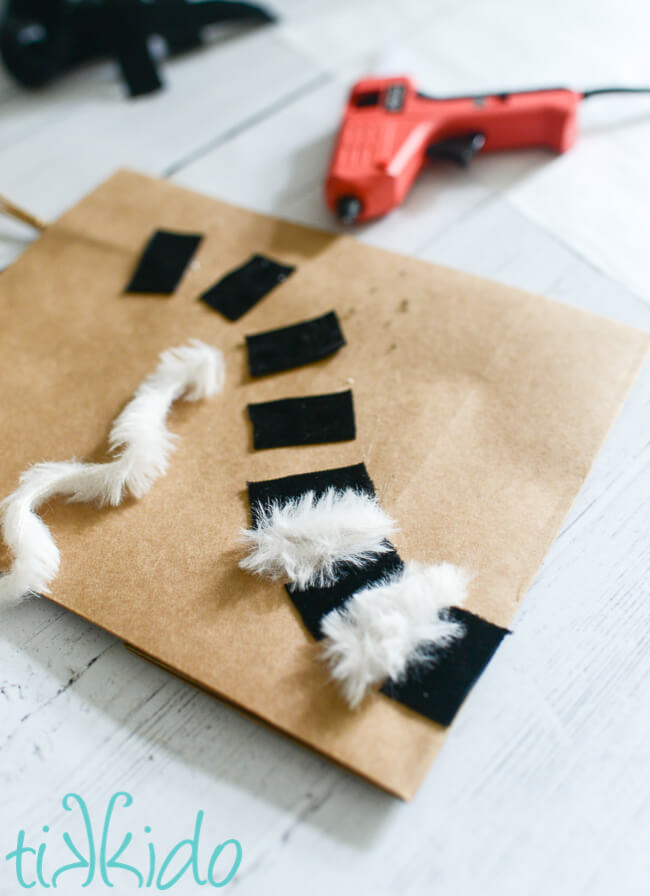 White furry eyelash yarn being glued between pieces of black velvet ribbon to create the lemur tail on a Lemur Gift Bag.