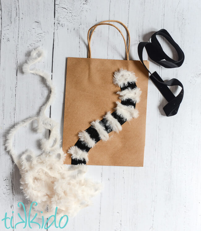 Black velvet ribbon and white furry yarn glued on a plain gift bag to make a Lemur Gift Bag.
